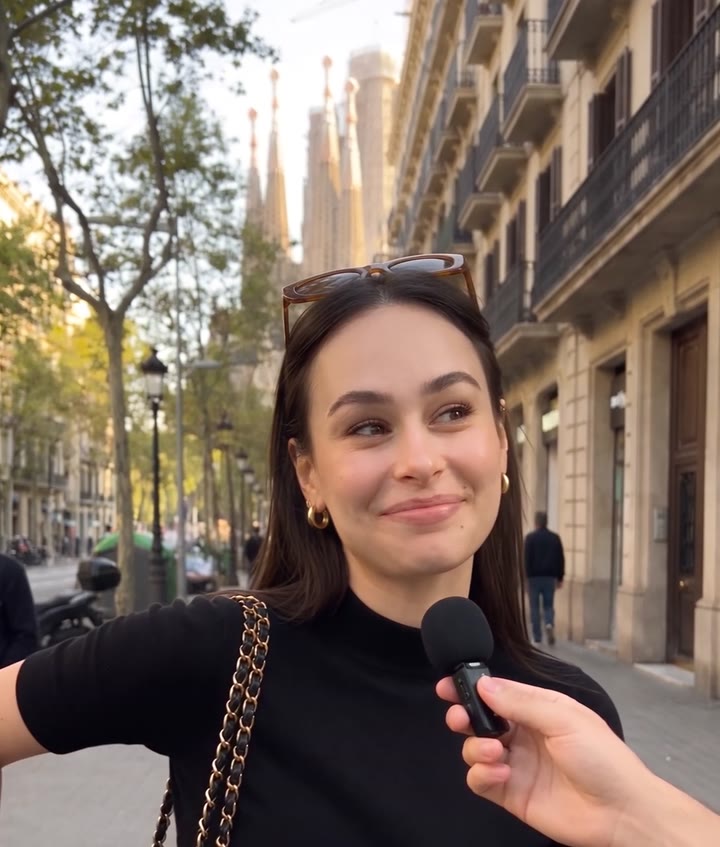 A young woman smiles at a handheld microphone on a Barcelona street